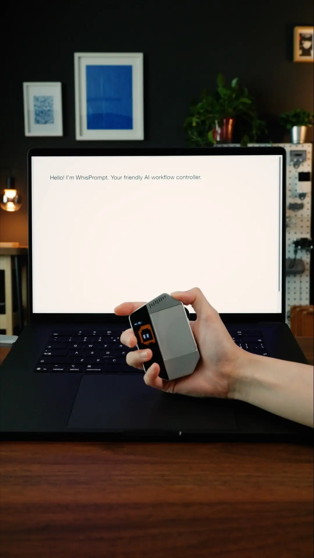 WhisPrompt AI workflow controller held in one hand in front of a laptop